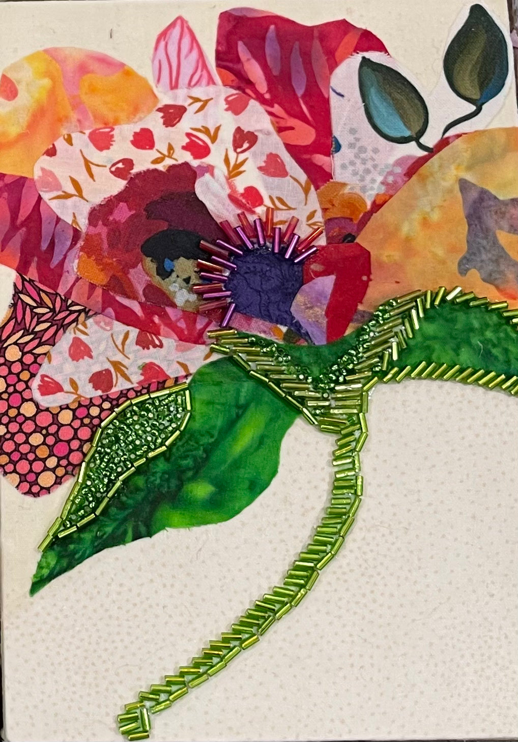 Botanical fabric mixed media wall art with colorful flower, green beaded stem, and layered textile petals