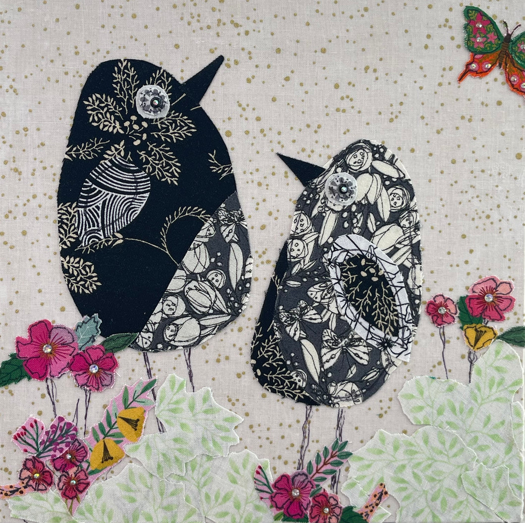 Textile bird art showing two black and white patterned birds surrounded by soft florals in a calm, minimalist composition