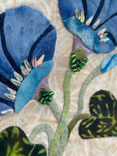Close-up of fabric with blue flowers and green leaves with beads and crystal details on a beige background
