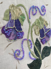 Close-up floral design with purple flowers and green leaves with beads and crystals on a beige background