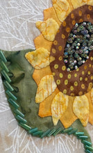 Close-up of a sunflower-shaped fabric piece with beaded center on a textured background