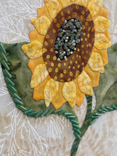 Decorative sunflower patch with bead center and leaves on a textured fabric background