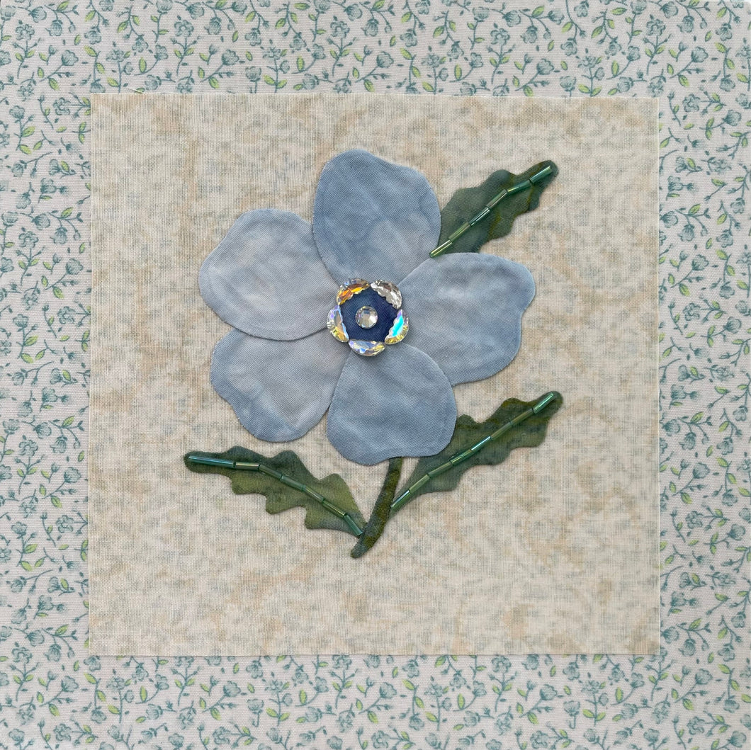 8 x 8 fabric collage artwork featuring a soft blue flower with crystal center and green stitched leaves made from inherited textiles