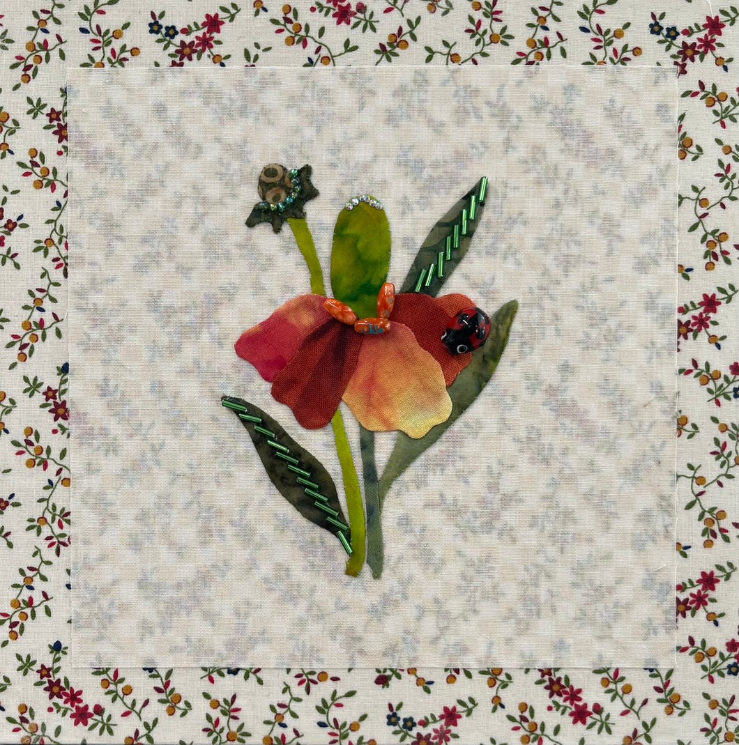 Floral quilt block with a red flower and green leaves on a textured fabric background.