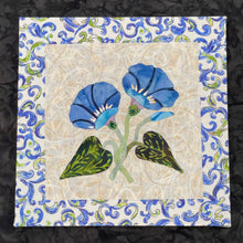 Hand-appliquéd blue floral textile artwork featuring two soft blue flowers with subtle bead and crystal accents on a neutral fabric background