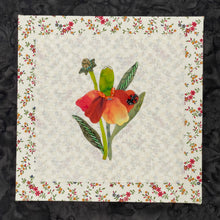 Hand-appliquéd floral textile artwork with orange and yellow petals, beadwork details, and a small ladybug on a neutral fabric background mounted on an 8x8 panel