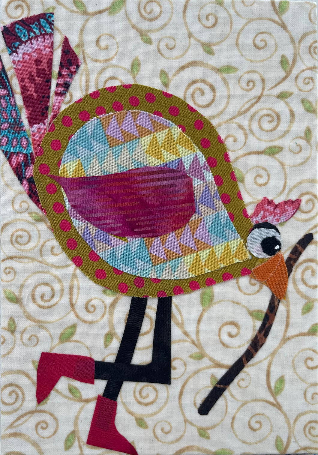 Whimsical fabric collage bird with colorful patterned body holding a walking stick, set against a soft swirling background