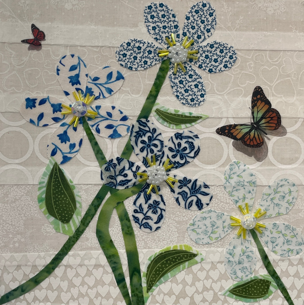 Fabric flower artwork with blue and white patterned blooms, green stems, and butterfly accents on 8x8 panel