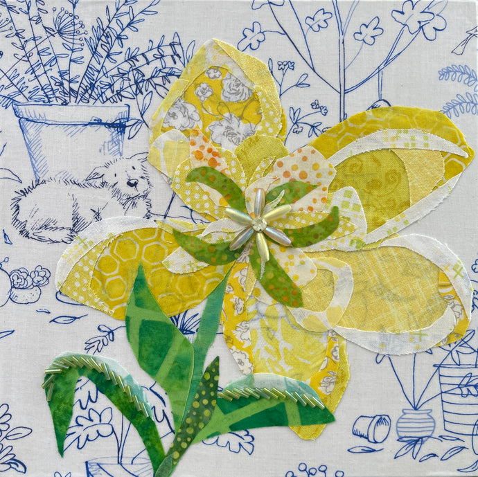 Yellow fabric flower artwork on 8x8 panel with layered textiles, beads and green leaves on illustrated botanical background