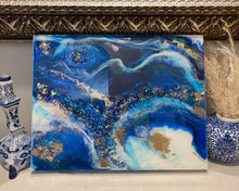 Abstract ocean artwork made with recycled glass and resin on a blue painted background, featuring textured waves and reflective details