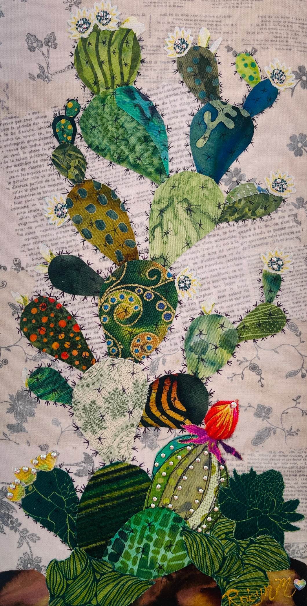 Original cactus fabric artwork 6x12 inches, prickly pear cactus in layered patterned batik fabrics teal gold olive orange with Swarovski crystal white flower centers ink pen spine detail single orange red bloom, vintage toile botanical text background warm brown ground, birch panel, Floral Botanical Collection, Robyn Moore Arts