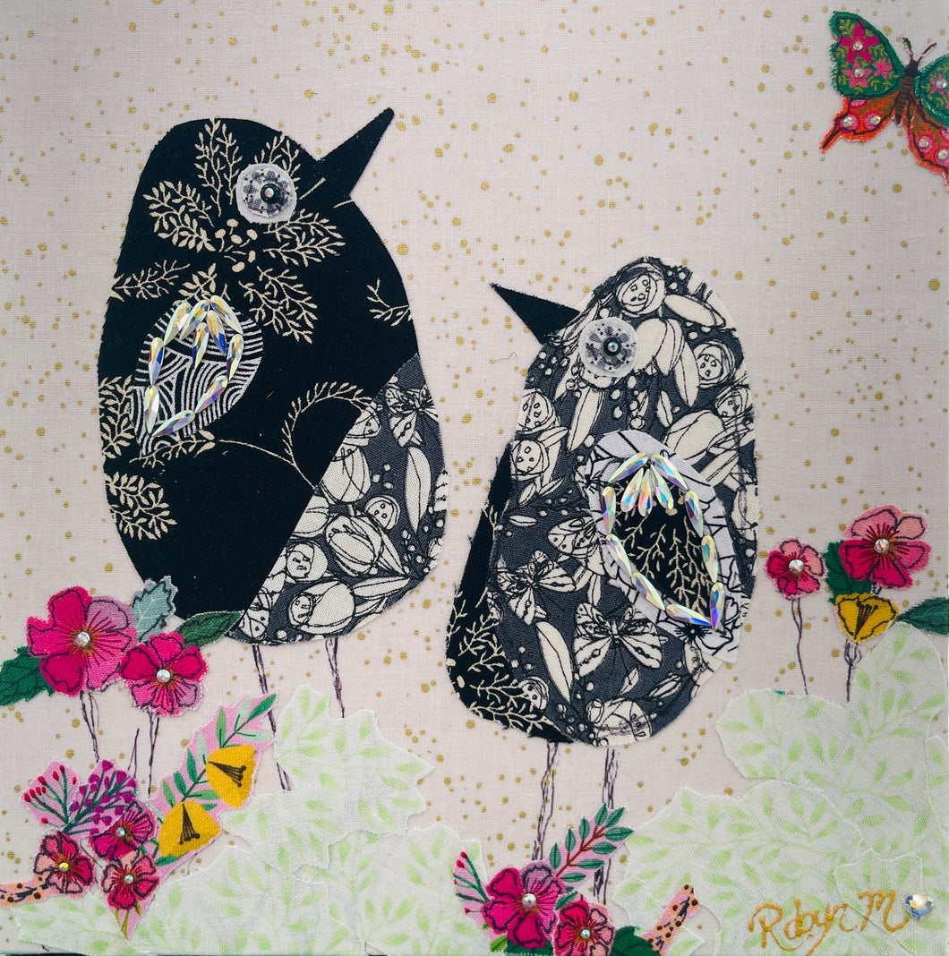 Textile bird art showing two black and white patterned birds surrounded by soft florals in a calm, minimalist composition