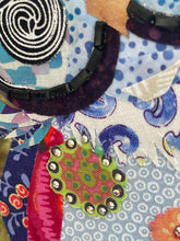Close detail of Czech glass bead eye ring and spiral fabric eye center on original whimsical owl artwork Perfectly Odd by Robyn Moore Arts, showing precise dark bead outline surrounding black white spiral printed fabric eye above patchwork blue lavender fabric owl body