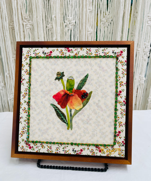 Floral quilt block with a red flower and green leaves on a textured fabric background.