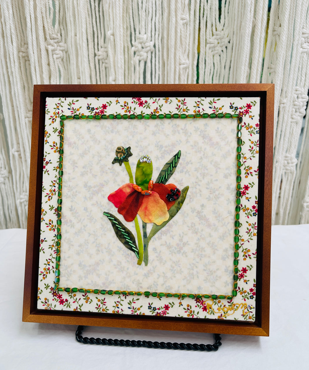 Floral quilt block with a red flower and green leaves on a textured fabric background.