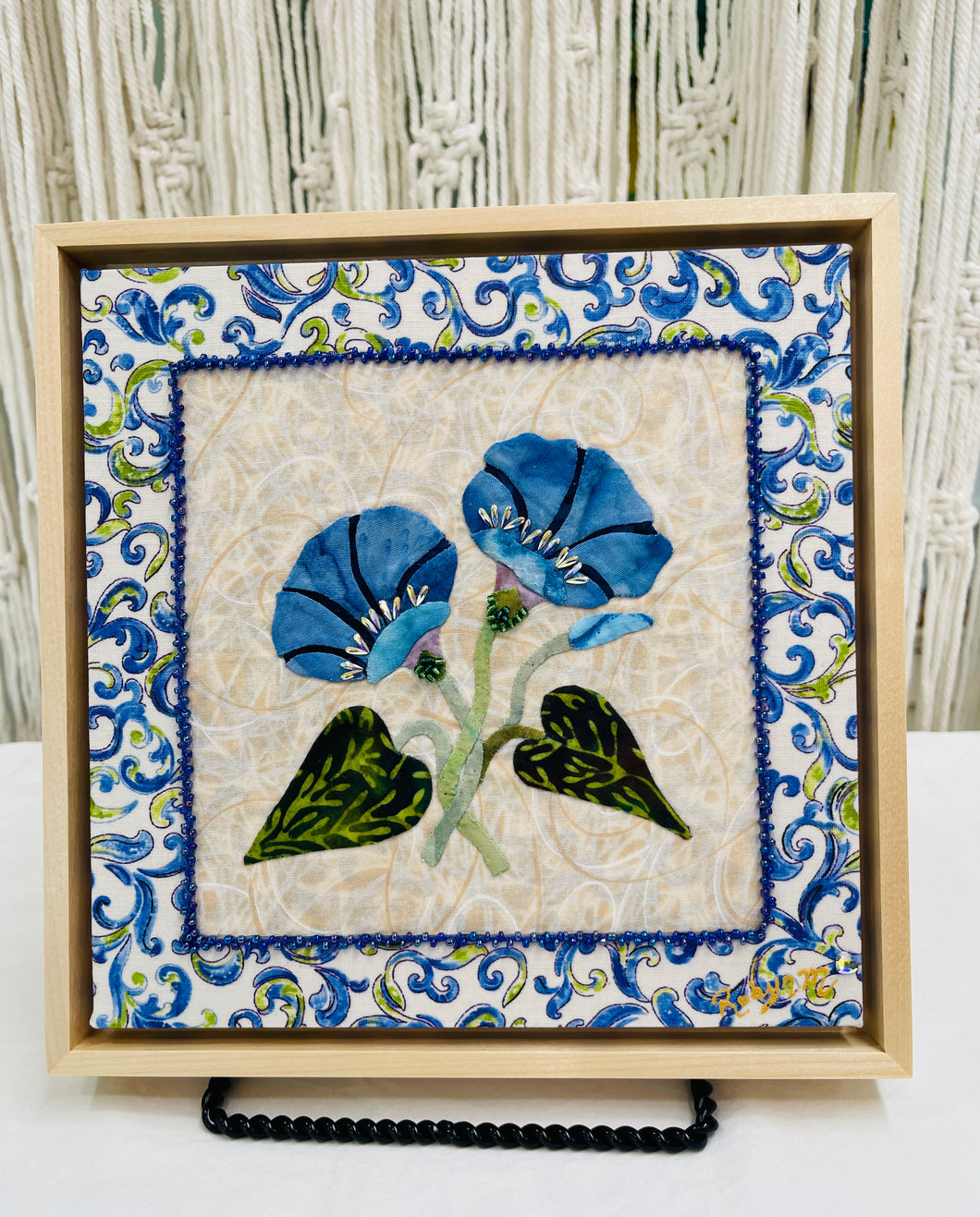 Artistic depiction of blue flowers and Swarovski crystals with green leaves on a textured beige background, surrounded by decorative blue floral patterns.