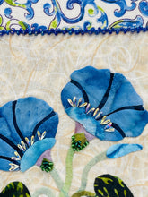 Close-up of fabric with blue flowers and green leaves with beads and Swarovski crystal details on a beige background