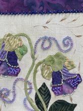 Close-up floral design with purple flowers and green leaves with beads and Swarovski crystals on a beige background