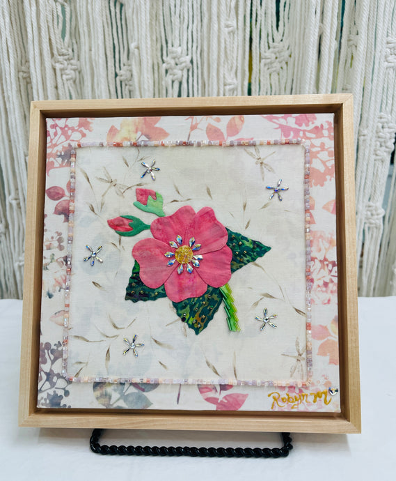 Coral pink fabric collage flower with Swarovski crystal center on neutral textile background, mixed media botanical artwork on birch panel