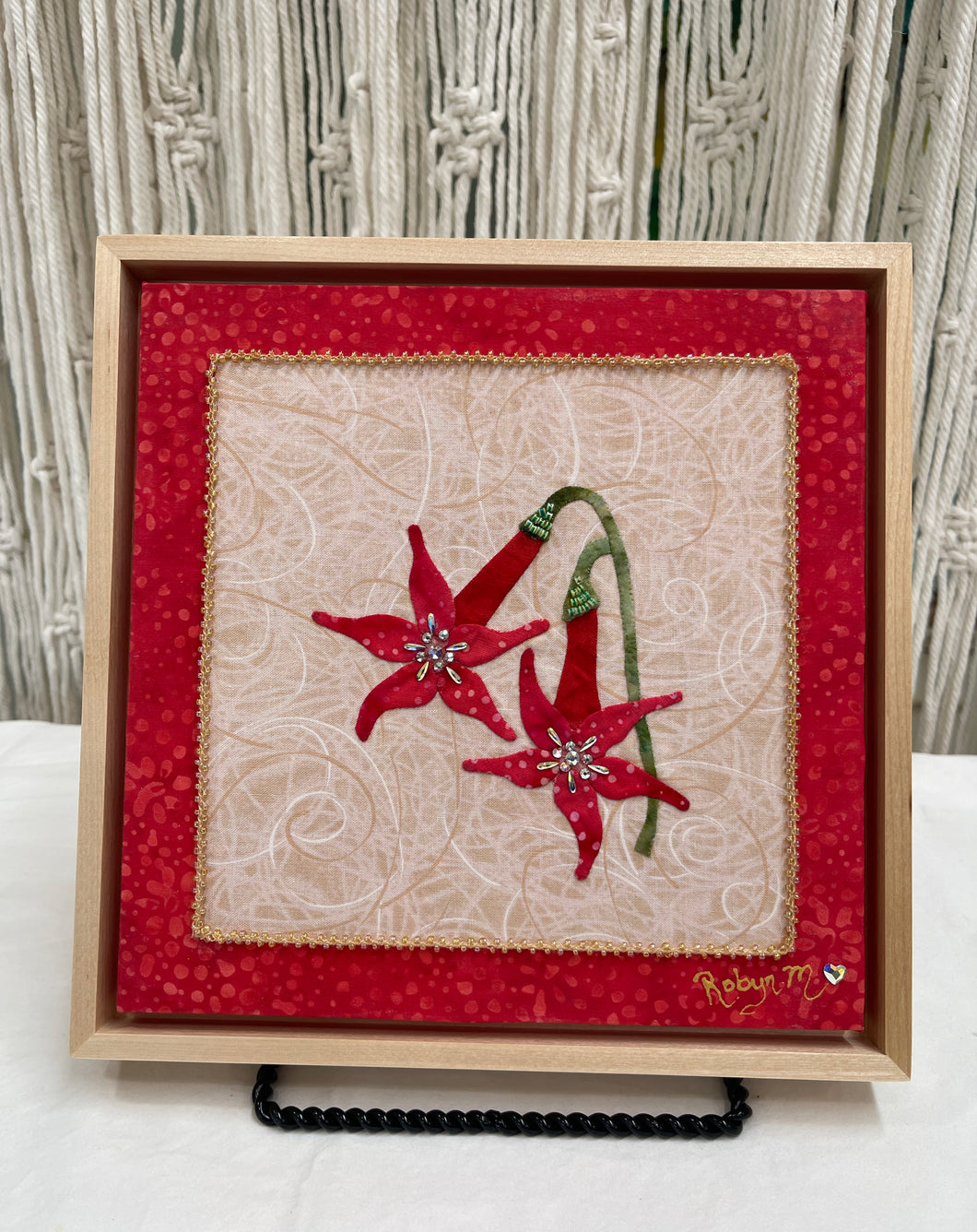 Two red fabric collage flowers with Swarovski crystal centers and green stems on a neutral textile background, mounted on an 8x8 panel