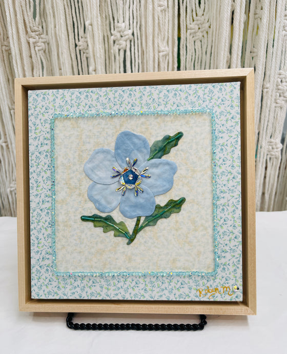 8 x 8 fabric collage artwork featuring a soft blue flower with crystal center and green stitched leaves made from inherited textiles