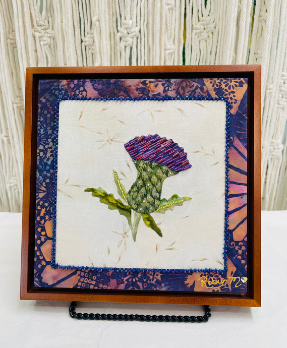 8 x 8 fabric collage artwork featuring a purple thistle flower with bead embellishments made from inherited textiles on neutral background