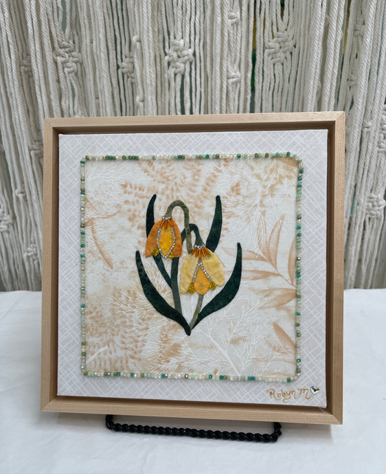 Yellow and gold bell-shaped fabric flowers with beadwork and Swarovski crystal detail on a soft neutral textile background, mounted on an 8x8 panel