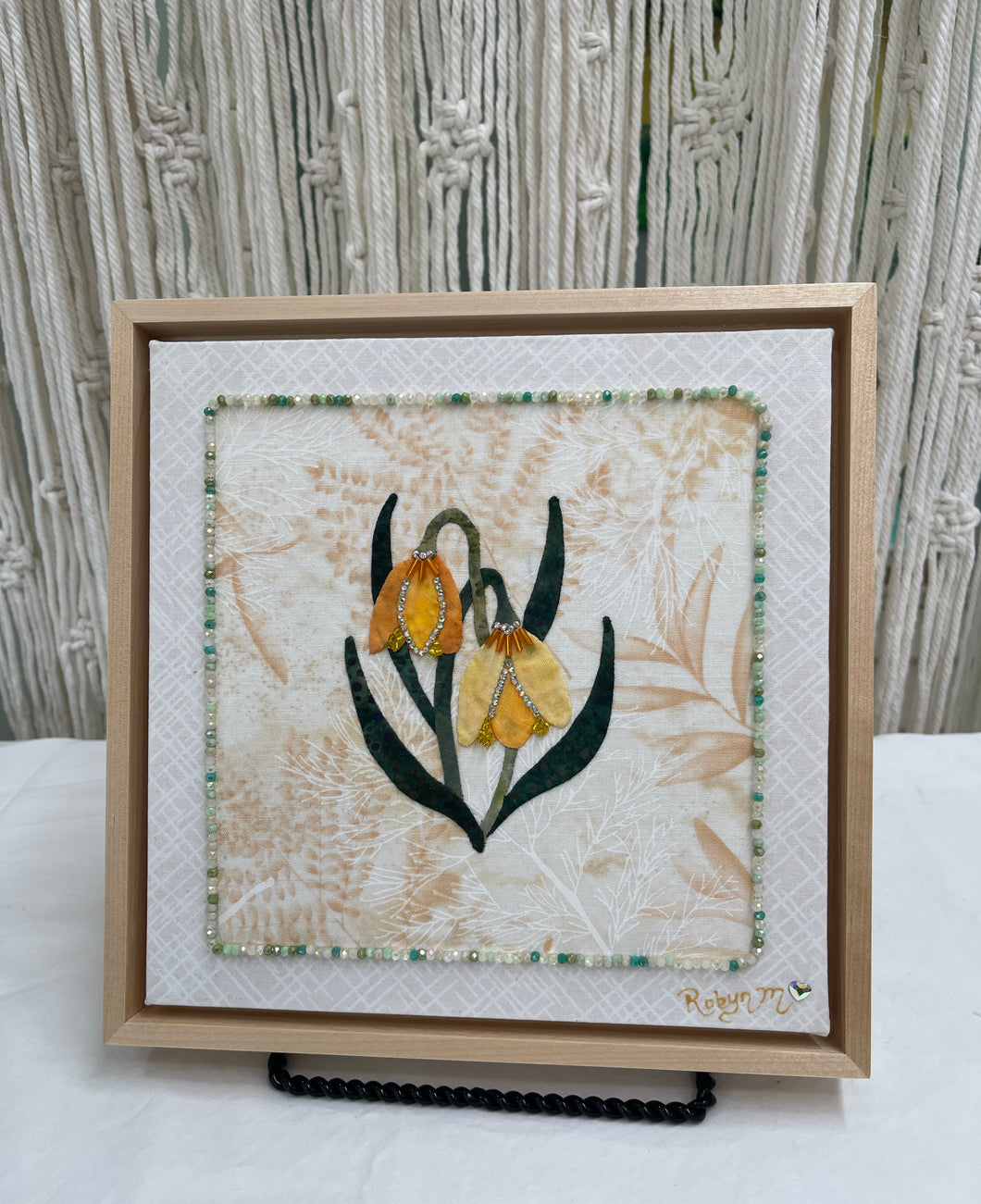 Yellow and gold bell-shaped fabric flowers with beadwork and Swarovski crystal detail on a soft neutral textile background, mounted on an 8x8 panel