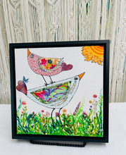 Whimsical bird artwork made with layered fabric and mixed media, featuring uplifting bird forms in soft neutral and warm tones in a grassy flower field