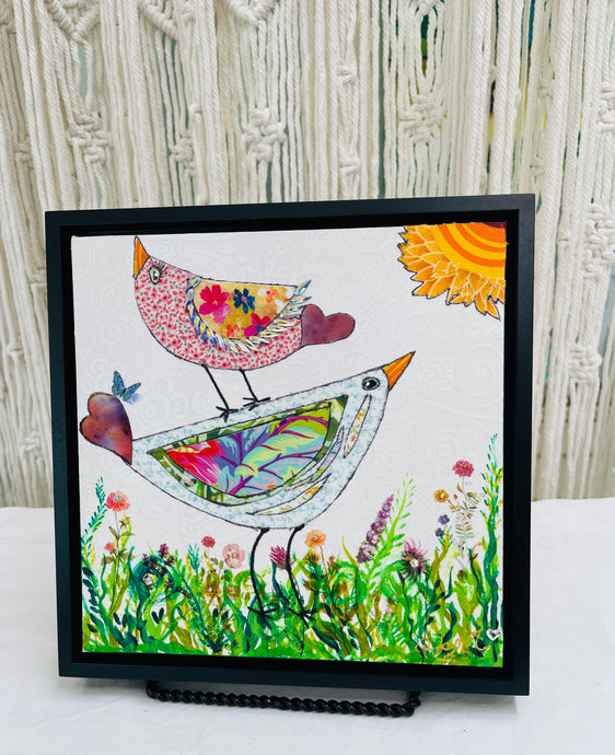 Whimsical bird artwork made with layered fabric and mixed media, featuring uplifting bird forms in soft neutral and warm tones in a grassy flower field