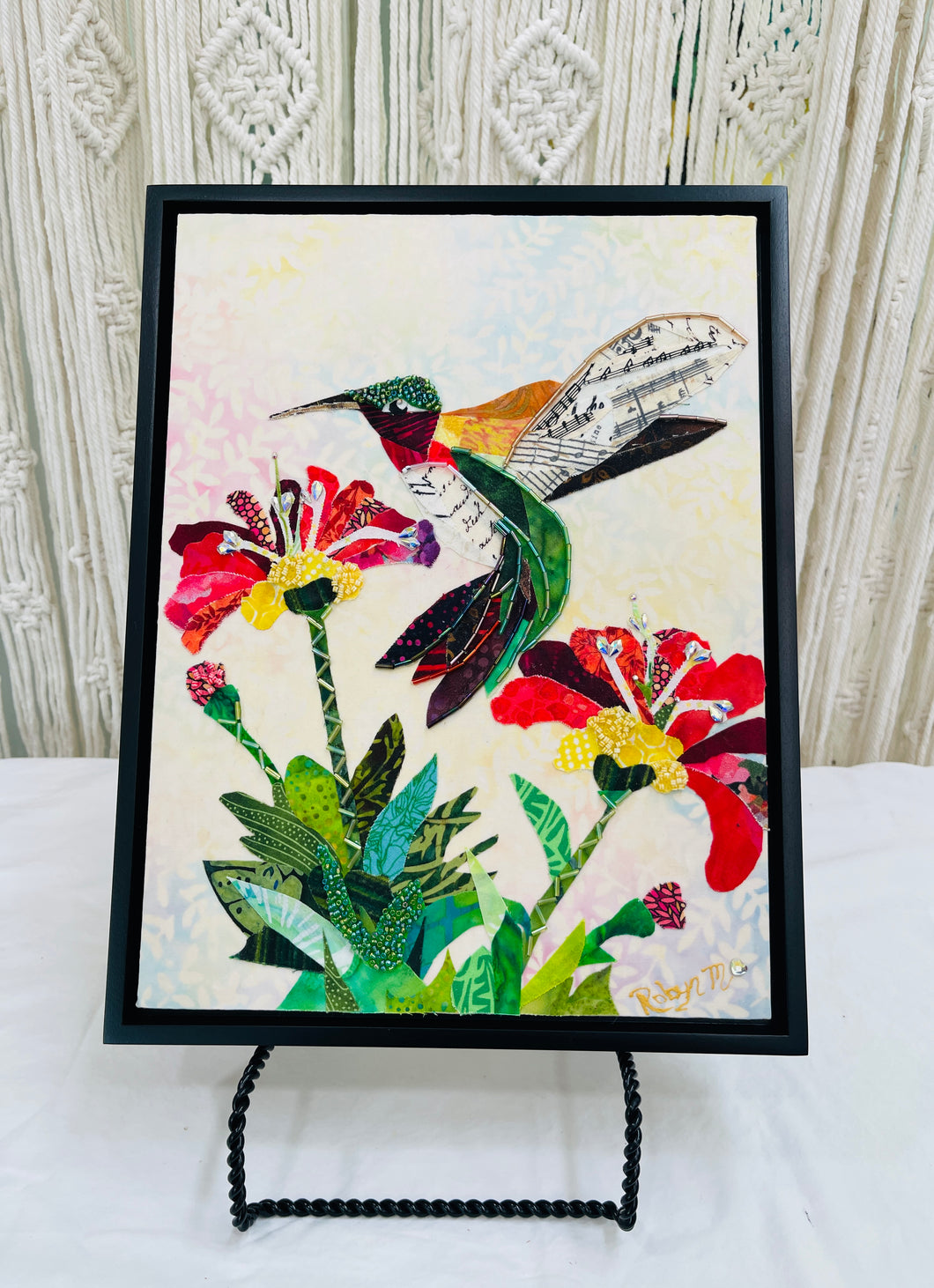 Original hummingbird fabric artwork 9x12 inches, ruby throated hummingbird in layered crimson teal gold batik fabric Czech glass bead head sheet music printed fabric wings Swarovski crystal flower centers lush green foliage, cream blush blue batik background, birch panel, Floral Botanical Whimsical Companions Collections, Robyn Moore Arts