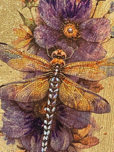 Close-up of a golden-brown dragonfly with crystal-accented wings resting among plum-toned florals on gold leaf.